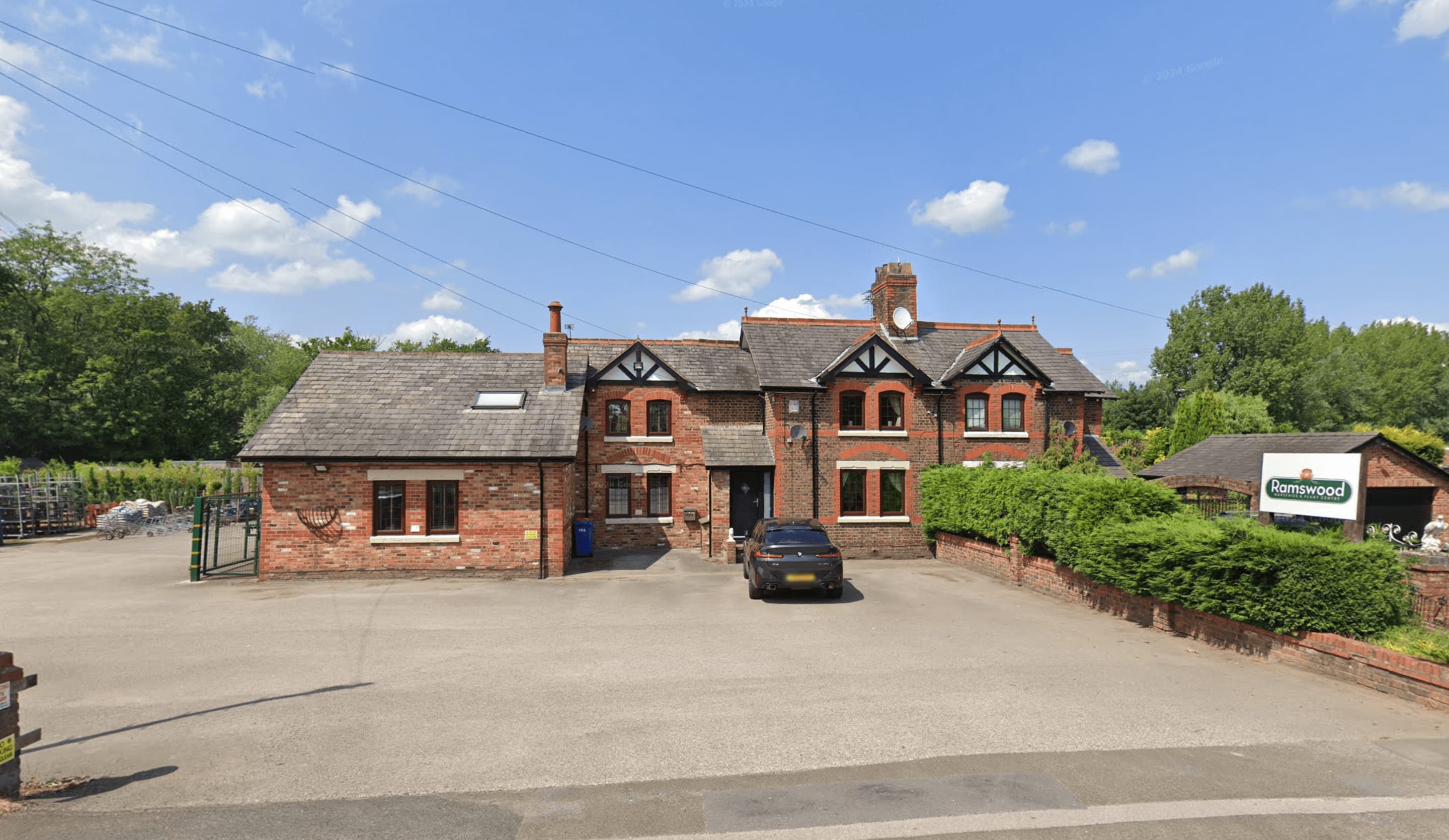 The front of Ramswood from the car park: a red-brick building with a gravel forecourt and a clipped hedge, and the Ramswood sign on the right, under a blue sky